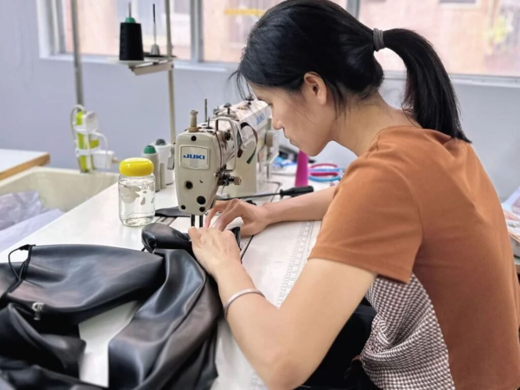 Workers operating industrial sewing machines inside a large clothing manufacturing factory in China producing garments